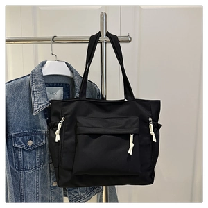 Detail of black nylon tote bag with white rope zippers and functional utility pockets