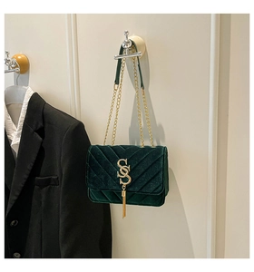 Detail of dark green velvet bag with V-quilted texture, gold SS logo and fringe tassel