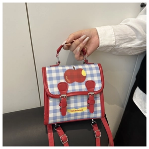 Detail of blue plaid mini backpack featuring red apple motifs and yellow strap accents