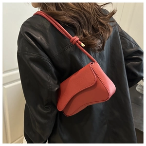 Chic red shoulder bag with asymmetrical flap and knot strap detail on black leather jacket