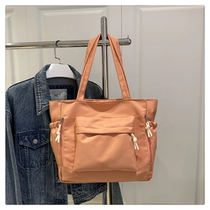 Detail view of apricot pink tote bag with multiple pockets and rope zippers on a hanger