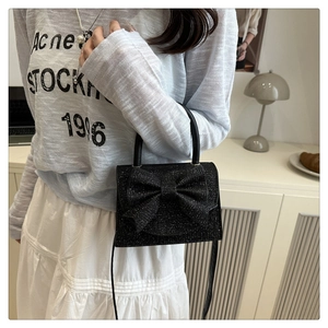 Detail of elegant black glitter evening bag featuring a large decorative bow and strap