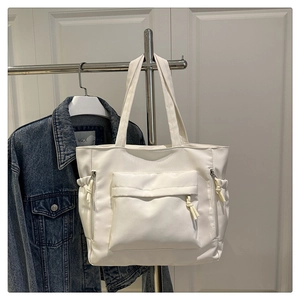 Detail showing white nylon tote bag with functional pockets and woven zip pullers