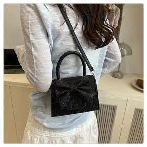 Detail of black glitter mini evening bag with large bow and circular metal handle