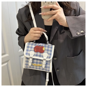 Detail of blue plaid crossbody bag with red apple pattern and buckle closures