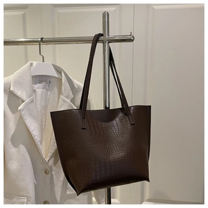 Detail of dark brown crocodile embossed tote bag hanging with white blazer outfit