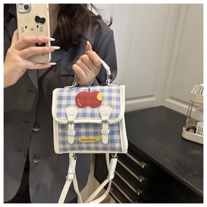 Detail of blue plaid mini handbag featuring a red apple graphic and white leather trim