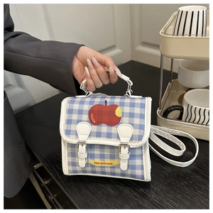 Detail of blue plaid crossbody bag with red apple print and double buckle closures