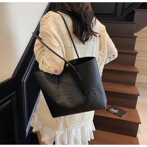 Detail of black leather tote bag with embossed TOTE BAG text and golden metal buckles
