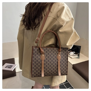 Detail of dark brown tote bag with M-pattern print and leather shoulder strap on a model