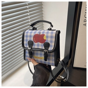 Detail view of a blue and white plaid handbag with a red apple print and black straps