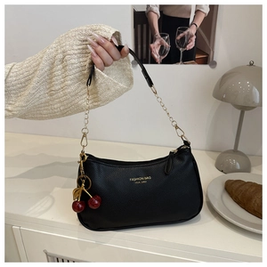 Detail of black lychee grain leather bag featuring gold chain and cherry charm detail