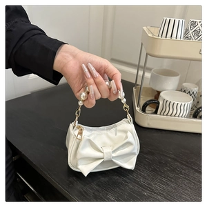Mini white leather bag with large bow and pearl handle on a minimalist shelf