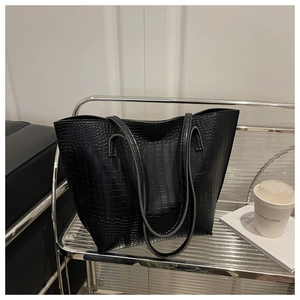Detail shot of black crocodile embossed leather tote bag on a modern metal display