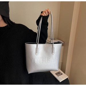 Detail of silver metallic tote bag with embossed lettering and shoulder strap handles