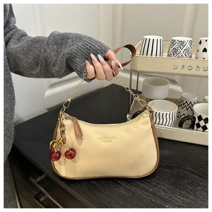 Detail view of cream lychee texture bag with gold chain and cherry charm on grey knit