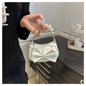 Close-up of white satin mini bag featuring a large bow and elegant pearl handle