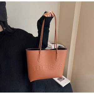 Detail of caramel brown tote bag featuring embossed TOTE BAG text and fine leather texture