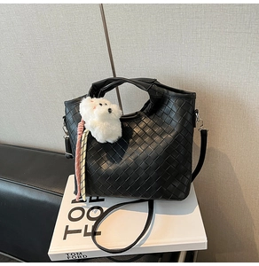 Detail of black woven shoulder bag with plush puppy pendant on textured surface