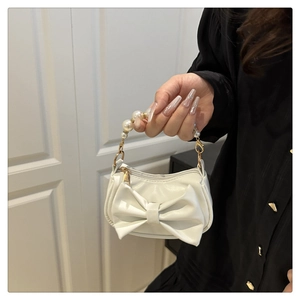 Detail of white mini handbag with large bow design and elegant pearl beaded handle
