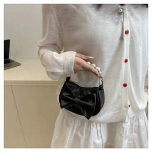 Detail of a chic black mini bag with a large bow and elegant pearl handle strap