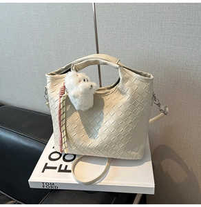 Detail view of cream woven bucket bag texture with plush puppy charm and strap