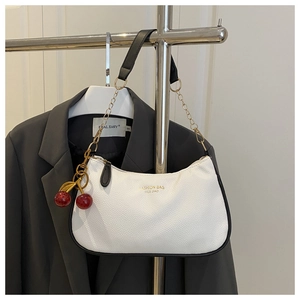 Detail of white half-moon bag featuring black trim and decorative cherry pendant detail