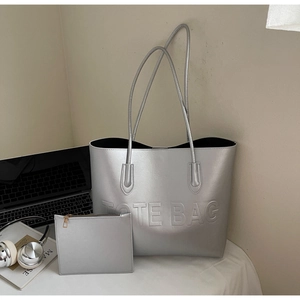 Detail of silver tote bag set with TOTE BAG embossed design on a desk with accessories