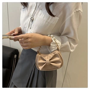Close-up of beige bow handbag featuring a large ribbon and elegant pearl bead handle
