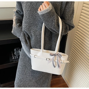 Dettaglio di una borsa sottobraccio bianca con un elegante fiocco a quadri in seta