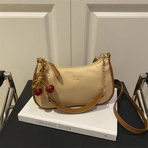 Fashion beige and brown underarm bag with cherry pendant on a white book surface