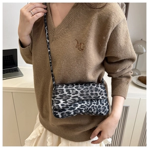 Detail of leopard print mini saddle bag worn over a brown knit sweater with white skirt