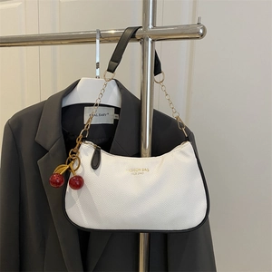 White pebbled leather shoulder bag with gold chain and red cherry charm on grey blazer
