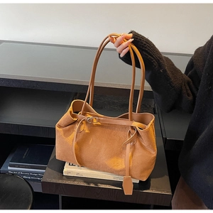 Detail of a brown suede tote bag featuring slim shoulder straps and a modern buckle strap