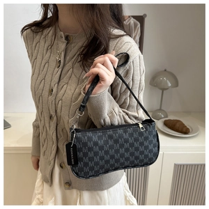 Detail of black underarm bag with M-pattern print and fashion tag on home background