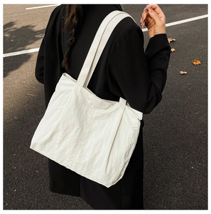 Detail of white nylon tote bag with crinkled texture and branding on black coat