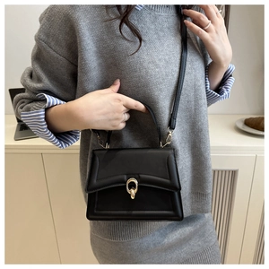Detail of minimalist black leather crossbody bag featuring a golden oval metal clasp