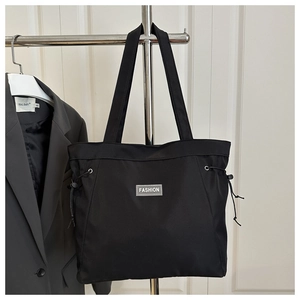 Detail of black nylon tote bag featuring fashion label and adjustable drawstring sides