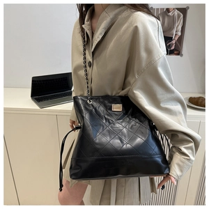 Detail of a black quilted tote bag with metal chain strap worn by a model in lifestyle setting