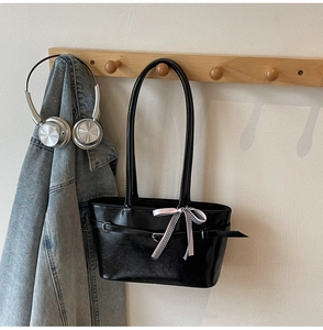 Dettaglio della borsa a spalla nera lucida con fiocco rosa su una gruccia in legno minimal