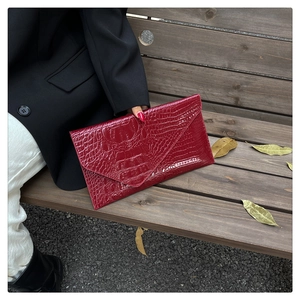 Detail of burgundy crocodile pattern envelope clutch bag held in an outdoor setting