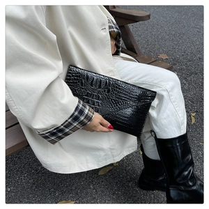 Detail of the high-gloss black crocodile embossed texture on a long leather clutch bag