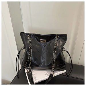 Detail of black quilted tote bag featuring glossy leather and gold metal buckle lock