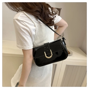 Macro view of vintage black patent leather shoulder bag with gold horseshoe buckle detail