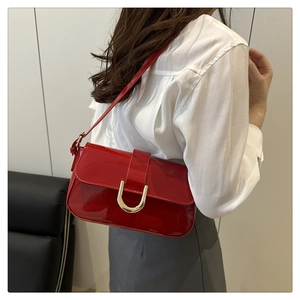 Detail of red patent leather shoulder bag with gold horseshoe buckle and glossy finish