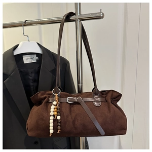 Detail of brown suede tote bag with leather buckle strap and wooden bead charm accessory