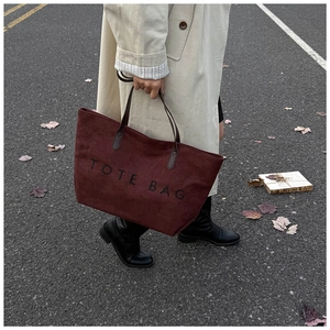 Detail of dark red suede tote bag with black TOTE BAG embroidery and brown handles