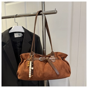 Close-up of brown suede tote bag with leather strap and decorative wooden bead charm