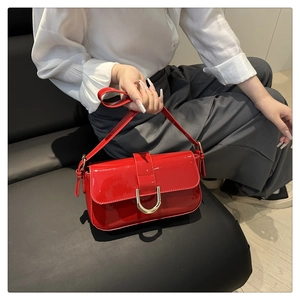 Close-up of bright red patent leather handbag with gold horseshoe buckle and flap cover