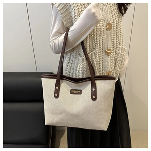 Detail of canvas tote bag with brown leather trim and golden logo tag on female model